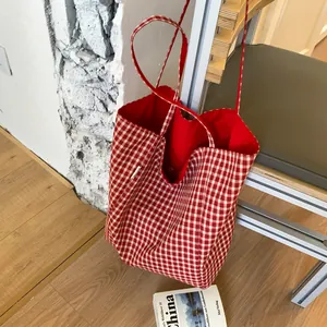 Large red and white gingham canvas tote bag with long straps on a minimalist chair