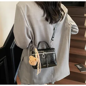 Detail of glossy pleated black handbag with cute plush bear charm and ribbon accent