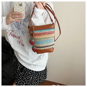 Detail of woven rainbow straw bucket bag with strawberry charms and leather strap