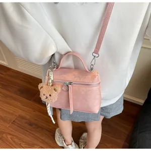 Detail of pink cracked texture box bag featuring a plush bear charm and metallic zipper