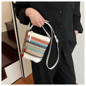 Detail of striped woven crossbody bag with white leather trim and strawberry charm