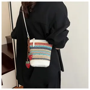 Detail of colorful woven bucket bag with white leather trim and red strawberry charms