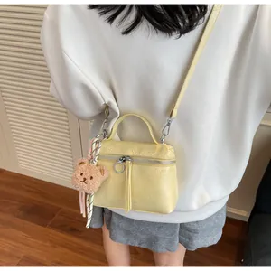 Detail of yellow pleated handbag with bear charm and long detachable shoulder strap