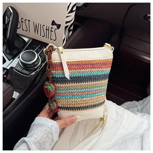 Detail of woven straw bucket bag with red strawberry charm and leather stitching