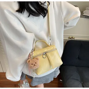 Detail of yellow patent leather lunch bag with plush bear charm and crossbody strap