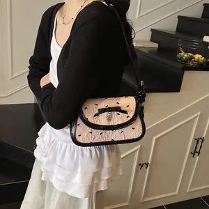 Pink shoulder bag with black bow patterns and a heart pendant in a lifestyle setting