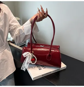 Detail of burgundy patent leather handbag with cherry pendant and pearl bow charm