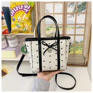 Détail du sac fourre-tout blanc avec nœuds noirs, bandoulière cuir et pendentif cœur