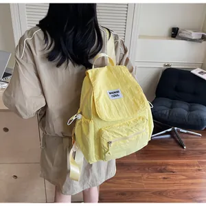 Detailed view of the yellow nylon backpack featuring white logo label and side drawstring pocket