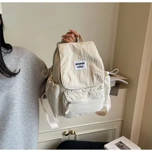 Detail of a minimalist cream-white backpack featuring a branded tag and drawstring side pockets