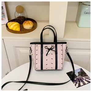 Détail du sac cabas rose à motif nœuds avec pendentif cœur sur une table de café