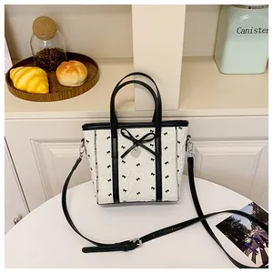 Détail du cabas en jacquard blanc avec nœuds en cuir noir et breloque en forme de cœur