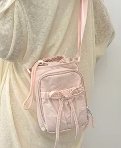 Sac bandoulière rose en nylon avec cordon et nœud, porté par un mannequin en détail