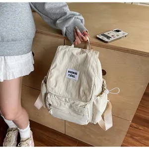 Detail view of cream nylon backpack with front logo patch and drawstring side pocket