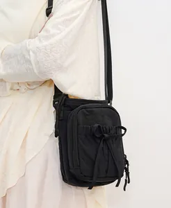 Détail du sac bandoulière en nylon noir avec nœud à cordon et poche zippée pratique
