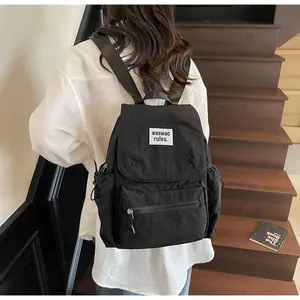 Close-up of a black minimalist nylon backpack featuring a white letter patch on stairs