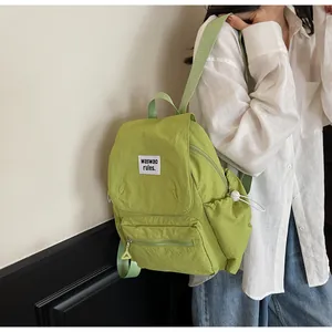 Detail of light green waterproof nylon backpack featuring a front zipper pocket and logo patch