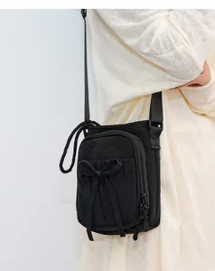 Vue de profil d'un sac bandoulière en nylon noir avec noeud sur un pull en maille beige