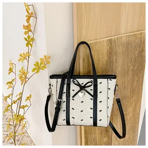 Détail du sac cabas gaufré blanc avec motifs nœuds noirs et pendentif cœur argenté