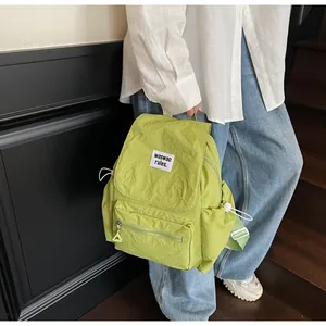 Detail of avocado green nylon backpack featuring 'waswac rules' patch and drawstring pockets