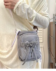 Détail d'un sac bandoulière gris avec nœud et tissu plissé porté par un modèle