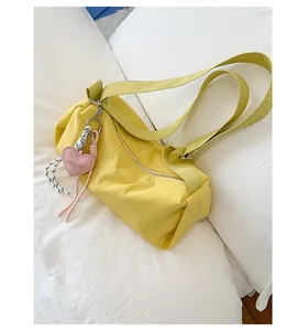 Detail of yellow nylon pillow bag featuring a pink heart charm and metal zipper closure