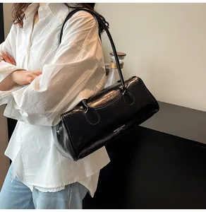 Detail of a black shiny leather cylindrical shoulder bag with fashion lettering