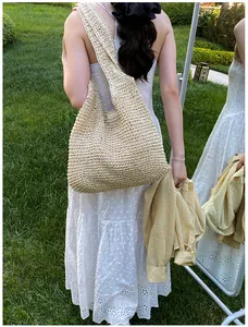Detailed texture of large handmade straw tote bag shown on grass in summer setting