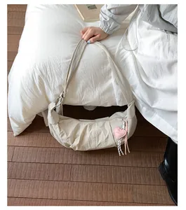 Detail der beigen sichelförmigen Tasche mit Reißverschluss und Herzanhänger auf Holzboden
