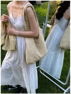 Detail of hand-woven beige straw tote bag with intricate white hollow embroidery dress