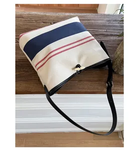 Detail of canvas tote bag showing striped pattern, horn buckle, and leather shoulder strap