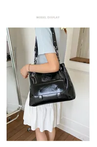 Detail of black glossy leather shoulder bag with metal chain strap and flap pocket detail