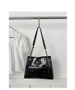 Vertical display of black glossy leather bag with silver chain strap and button pocket