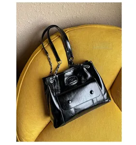 Detail view of a black glossy faux leather tote bag on a vibrant yellow corduroy chair