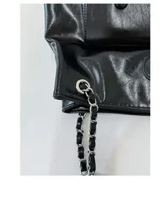 Detail of glossy black faux leather texture and silver chain strap weave on a stylish bag