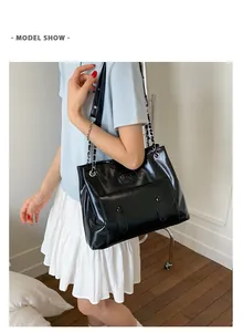 Close-up of black glossy tote bag with metal chain strap and front flap pocket detail