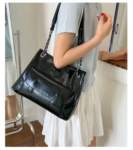 Detail of glossy black faux leather tote with metal chain strap and flap pocket