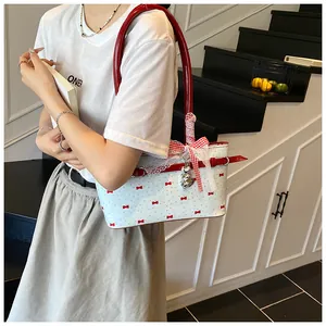 Détail de l'imprimé nœud rouge, bordure en dentelle blanche et pendentifs cœur en argent du sac