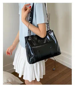 Close-up of black glossy tote bag showing flap pocket and embossed logo detail