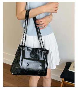 Detail of black glossy tote bag with silver chain strap and front flap pocket on a model