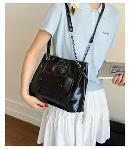 Detail of black glossy PU shoulder bag with metal chain strap and flap front pocket