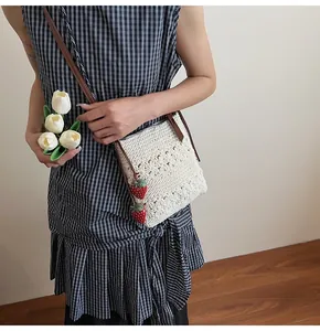 Detail of hollow woven crossbody bag featuring red strawberry charms and leather strap
