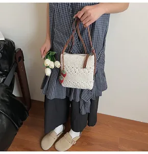 Close-up of woven cream crossbody bag with detailed floral texture and red strawberry charms