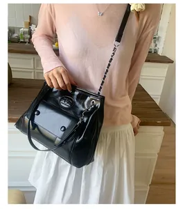 Detail of glossy black leather handbag with chain strap and logo on a pink outfit