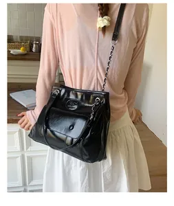 Detail of black glossy tote bag featuring a front flap pocket and metal chain strap