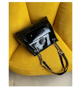 Detail of black glossy leather tote bag with metal logo and classic chain shoulder strap