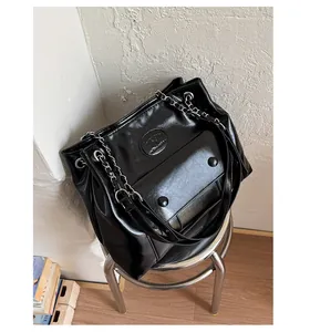 Detail of black glossy faux leather tote bag with silver chain strap on metal stool