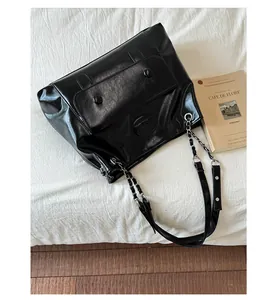 Detail of glossy black leather shoulder bag with silver chain strap and flip cover