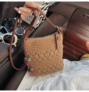 Detail of hollow woven shoulder bag featuring red strawberry charms and leather zipper pull