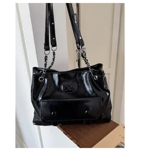 Detail of black glossy tote bag featuring silver chain straps and embossed logo front pocket